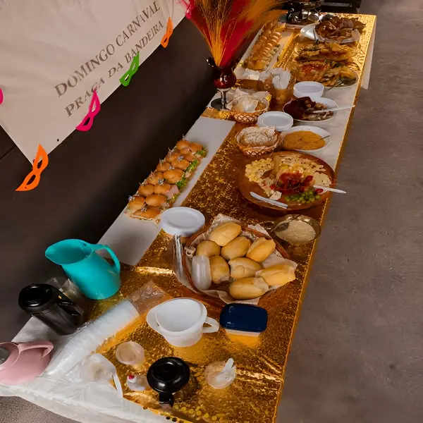 Mesa de buffet decorada com toalha dourada brilhante, servindo uma variedade de alimentos, incluindo sanduíches, pães, salgados e pratos prontos
